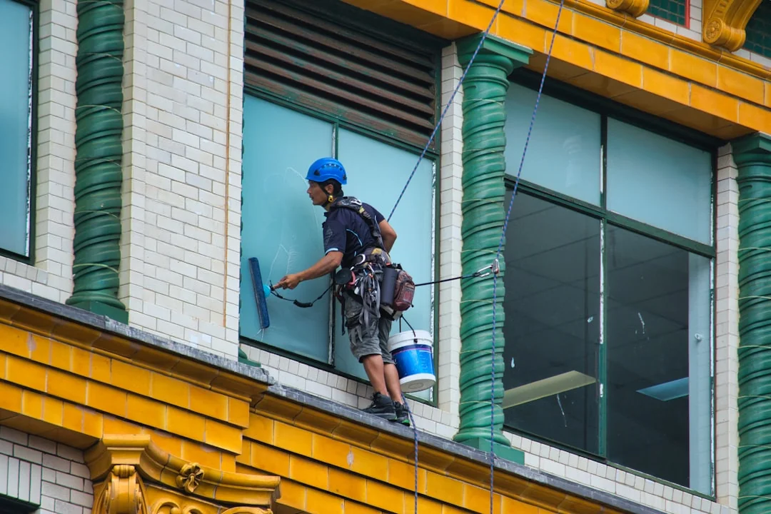 Close-up of hand cleaning window with squeegee outdoors using yellow gloves.
